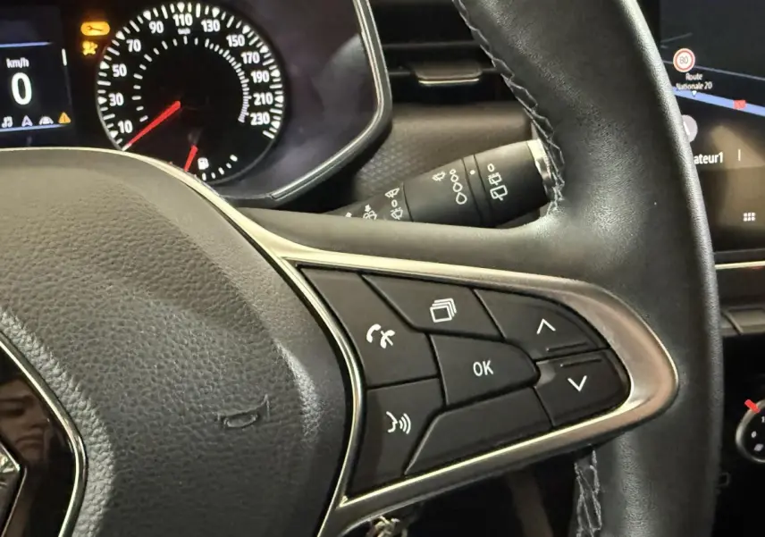 Gros plan sur le volant cuir synthétique de la Renault Clio Business blanc 2021 avec commandes multifonctions et tableau de bord numérique.