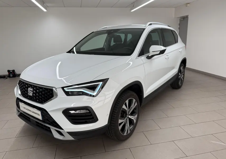 Vue 3/4 avant droite d'un SEAT Ateca blanc Nevada 2023 avec jantes alliage et calandre noire en intérieur showroom.