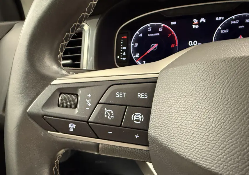 Gros plan sur les commandes au volant gauche du SEAT Ateca blanc Nevada, avec tableau de bord numérique en arrière-plan.