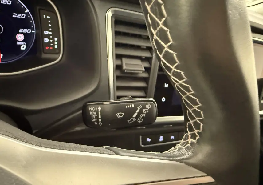 Gros plan sur la manette d’essuie-glace à gauche du volant noir avec surpiqûres blanches dans un SEAT Ateca blanc Nevada 2023.