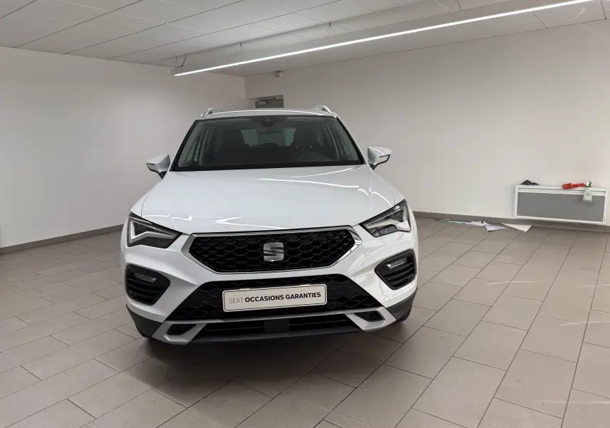 Vue avant d'un SEAT Ateca blanc Nevada 2023 dans un showroom, avec calandre noire et feux LED distinctifs.