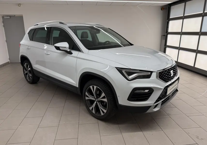 SEAT Ateca blanc Nevada en 3/4 avant droit, avec jantes alliage et toit avec barres de toit visibles.