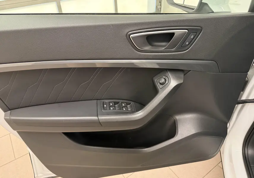 Vue rapprochée de la porte avant gauche du SEAT Ateca blanc Nevada, avec commandes de vitres et poignée intégrée.