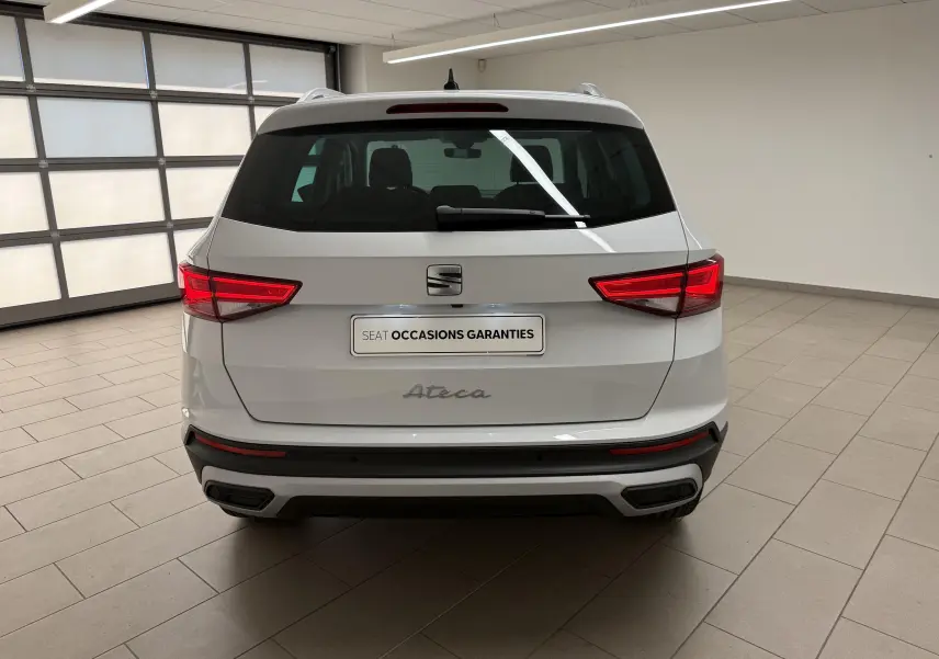 Vue arrière d'un SEAT Ateca blanc Nevada 2023 dans un showroom, avec feux arrière allumés et plaque "Occasions garanties".