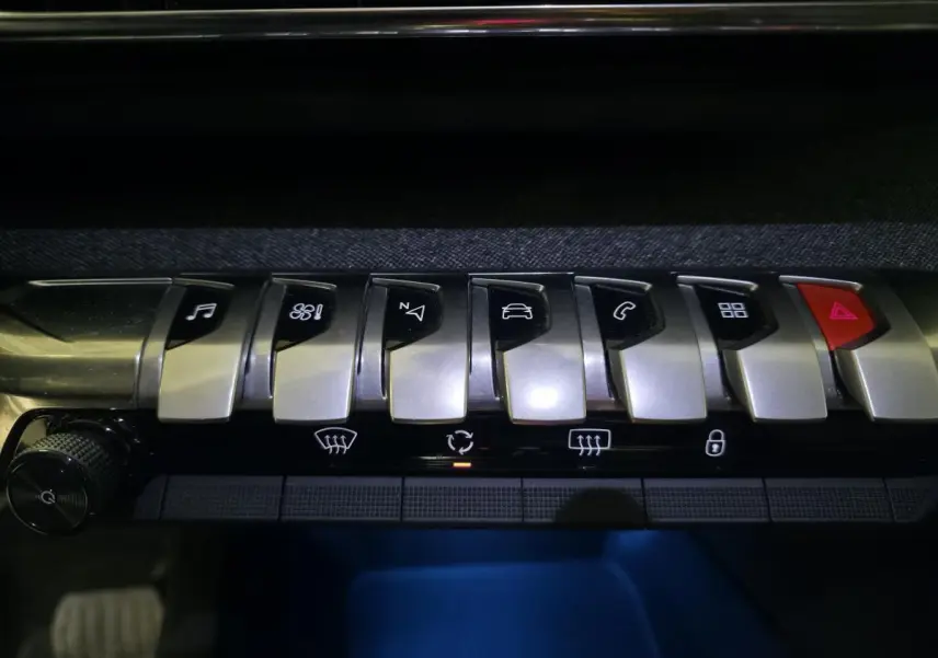 Gros plan sur les commandes en métal brossé de la console centrale du Peugeot 5008 gris, avec éclairage d'ambiance bleu.