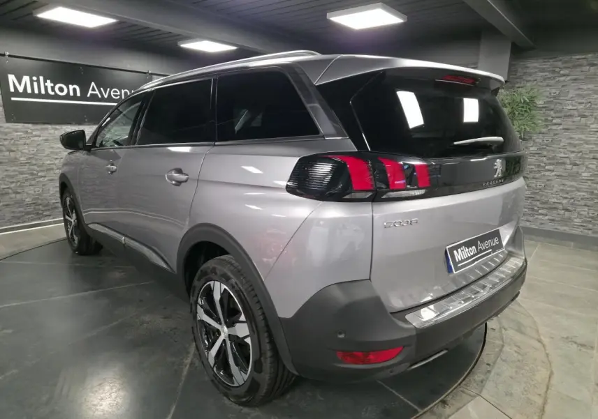 Vue 3/4 arrière droite d’un Peugeot 5008 gris métallisé avec jantes alliage bi-ton et vitres surteintées en intérieur showroom.