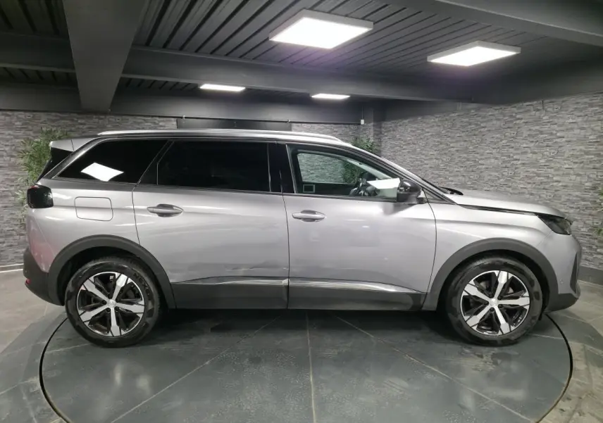 Profil droit du Peugeot 5008 gris métallisé 2022 avec jantes alliage bi-ton et vitres surteintées en intérieur showroom.