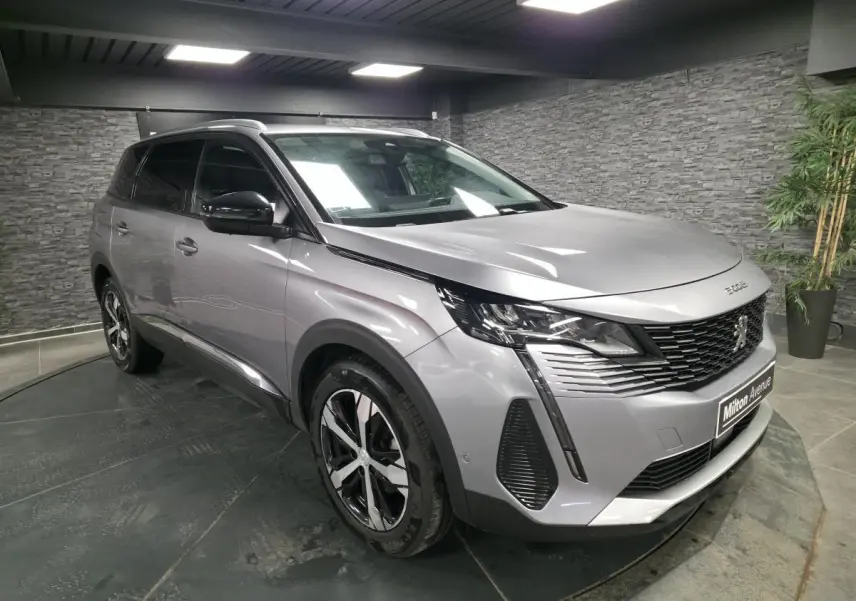 Peugeot 5008 gris métallisé vue 3/4 avant droit en intérieur avec jantes alliage bi-ton et calandre noire.