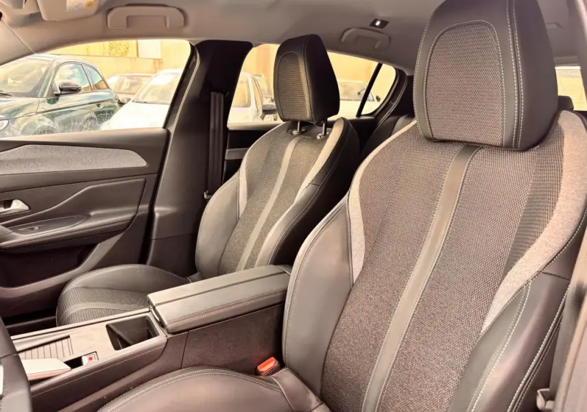 Vue intérieure côté avant droit du Peugeot 308 Hybrid 145 gris, avec sièges tissu et cuir, accoudoir central et port USB.