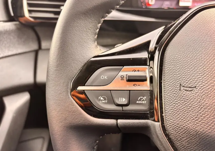 Gros plan sur les commandes à gauche du volant cuir noir du Peugeot 308 Hybrid 145 e-DCS6 Allure 2025.