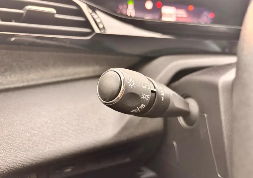 Gros plan sur la commande d’éclairage à gauche du volant dans l’habitacle gris du Peugeot 308 Hybrid 145 e-DCS6 Allure 2025.