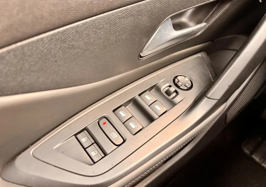 Vue rapprochée de la porte côté conducteur d'une Peugeot 308 gris, montrant les commandes électriques des vitres et des rétroviseurs.