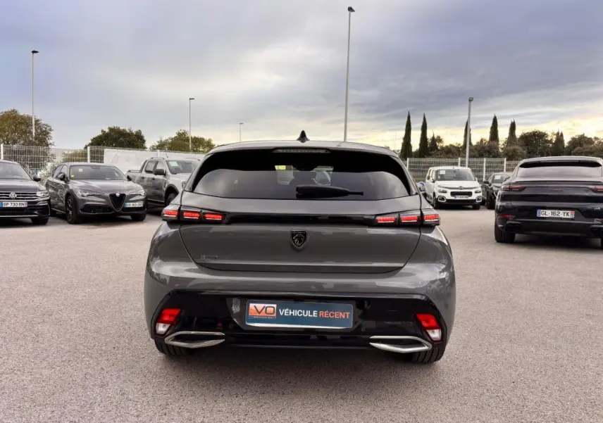 Vue arrière d'une Peugeot 308 Hybrid 145 gris métallisé, avec feux LED allumés et double sortie d'échappement chromée.