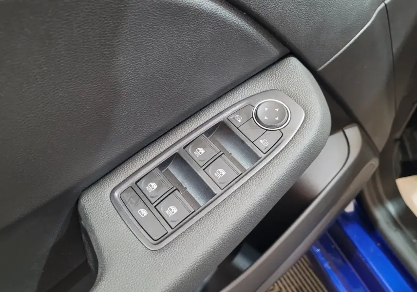Gros plan sur les commandes des vitres et rétroviseurs sur la porte côté conducteur d'une Renault Clio bleu 2025.
