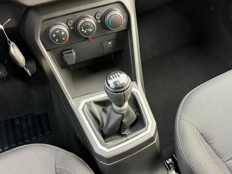 Vue intérieure centrée sur le levier de vitesses manuel de la Dacia Sandero blanche, avec commandes de climatisation visibles.