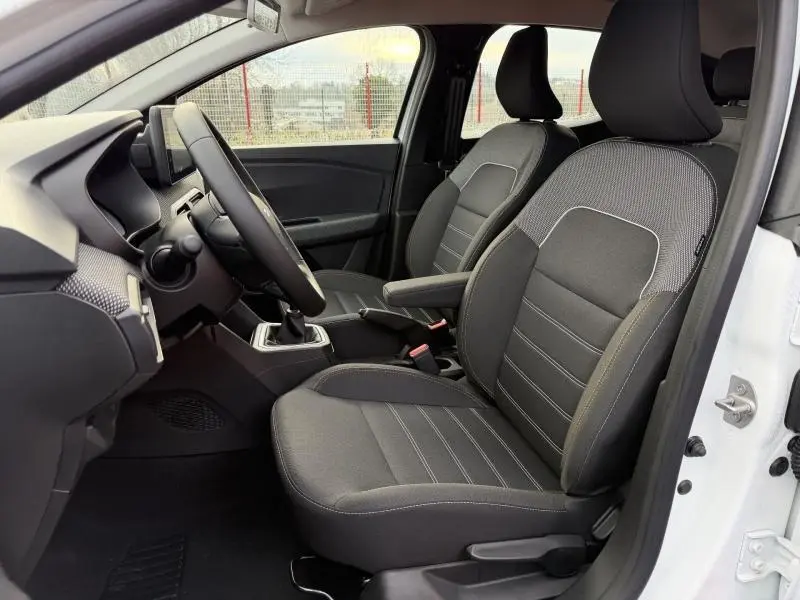 Vue intérieure côté gauche du Dacia Sandero blanc 2025, montrant les sièges avant en tissu gris et la boîte manuelle.