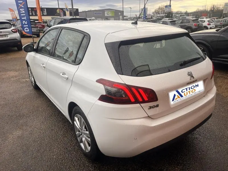 Vue 3/4 arrière droite d'une Peugeot 308 blanche Banquise avec feux arrière LED et jantes alu sur parking.
