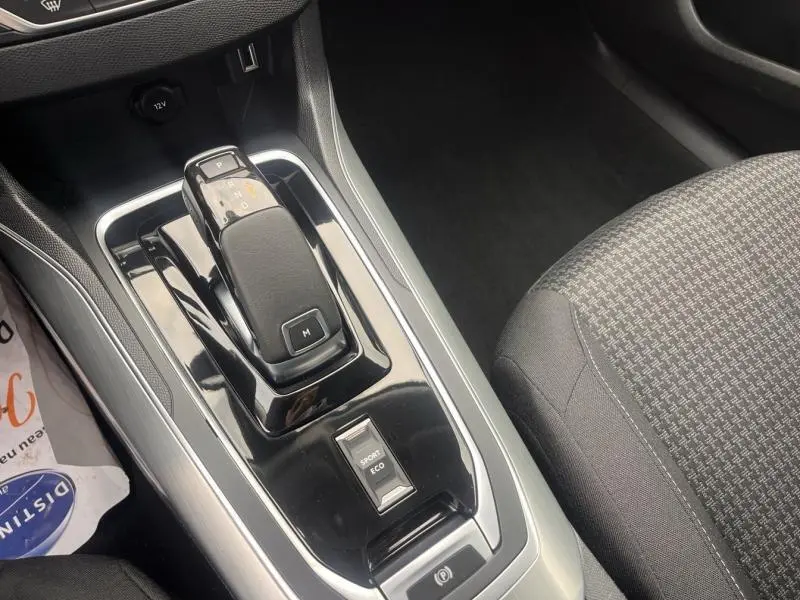 Vue rapprochée du levier de vitesses automatique noir et gris dans l’habitacle de la Peugeot 308 blanche, siège tissu gris visible.