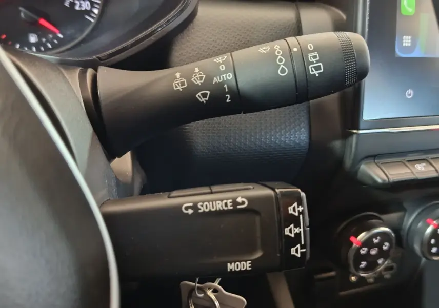 Gros plan sur les commandes au volant et la manette d’essuie-glace d’une Renault Clio gris clair, tableau de bord partiel visible.