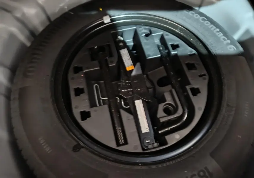 Gros plan sur la roue de secours et ses outils intégrés, sous le coffre d'une Renault Clio gris clair 2023.