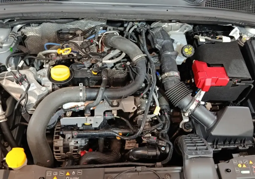 Vue rapprochée du moteur essence gris clair de la Renault Clio 2023 avec éléments jaunes et boîte à fusibles rouge visible.