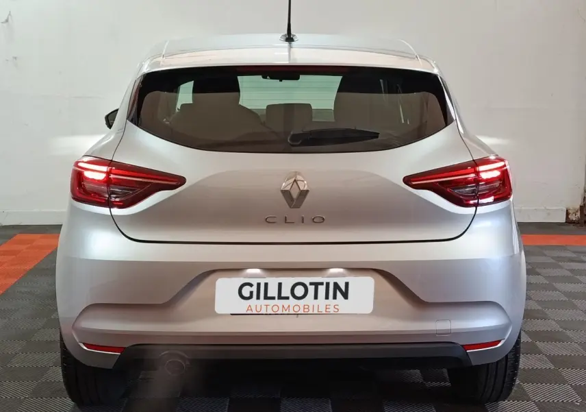Vue arrière d'une Renault Clio gris clair 2023 avec feux LED allumés et logo centré sur le hayon.