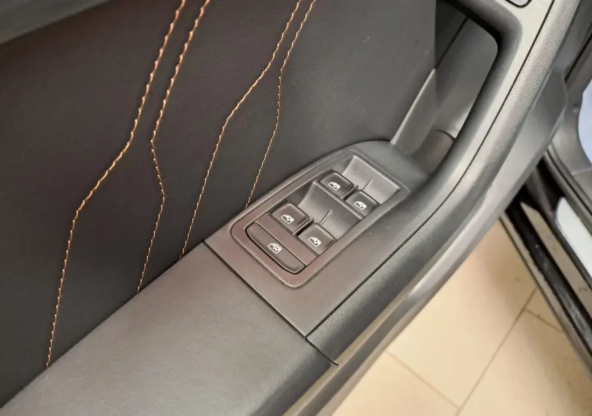 Gros plan sur la commande des vitres côté conducteur du CUPRA Ateca 2024, avec surpiqûres orange sur garniture noire.