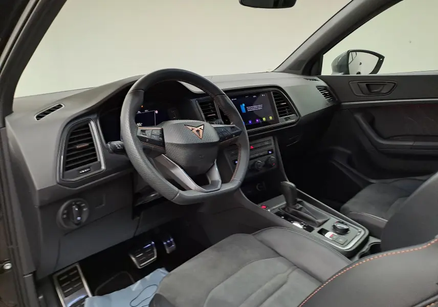 Intérieur du CUPRA Ateca 2024 vu côté conducteur, volant cuir noir avec logo cuivré et finition noire avec surpiqûres orange.