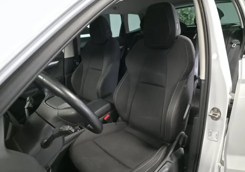 Vue intérieure côté conducteur du Skoda Karoq blanc 2024, sièges tissu noir et volant multifonctions.