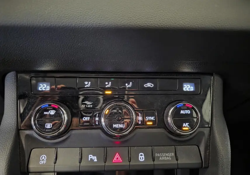 Détail de la console centrale noire avec commandes de climatisation automatique bi-zone et boutons de sécurité du Skoda Karoq blanc.