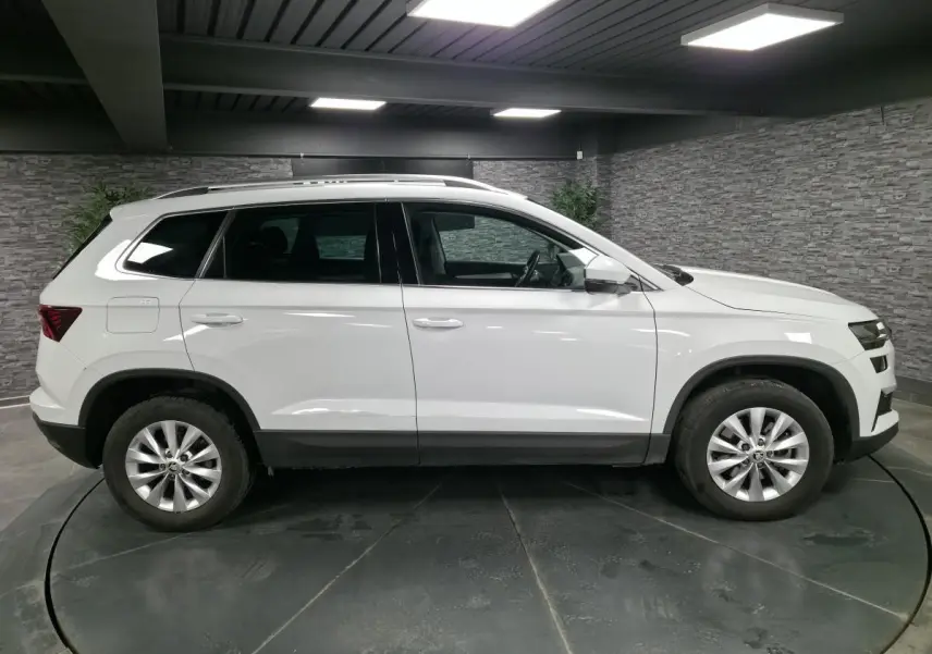 Vue latérale droite du SUV blanc Skoda Karoq 2024 avec jantes alliage et protections noires sur les passages de roues.