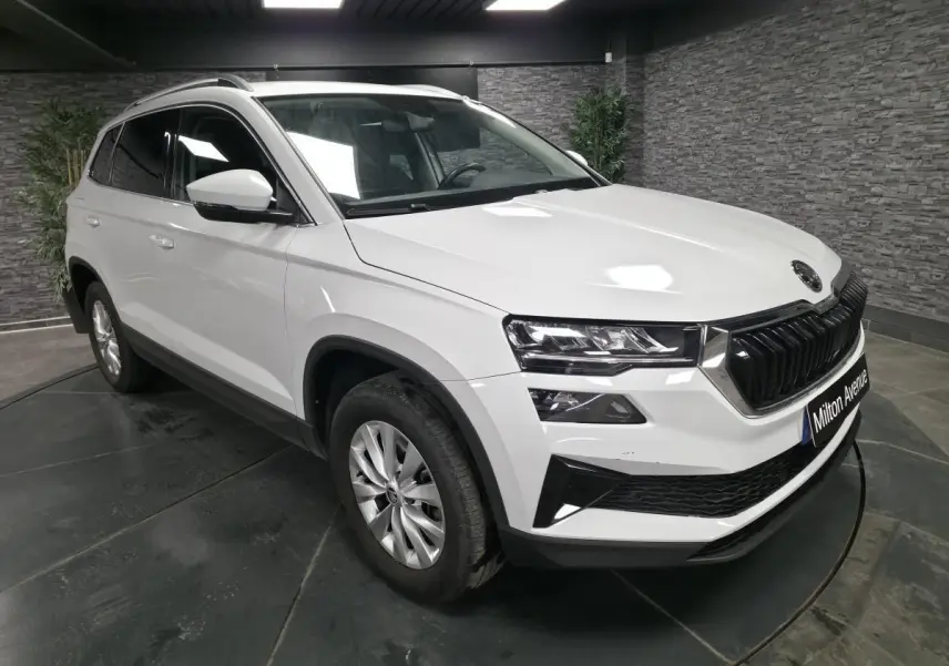 SUV Skoda Karoq blanc en 3/4 avant droit avec calandre noire et jantes alliage 16 pouces dans un showroom.