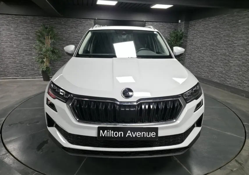 Vue frontale d'un SUV Skoda Karoq blanc 2024 avec calandre noire et plaque "Milton Avenue" en intérieur showroom.