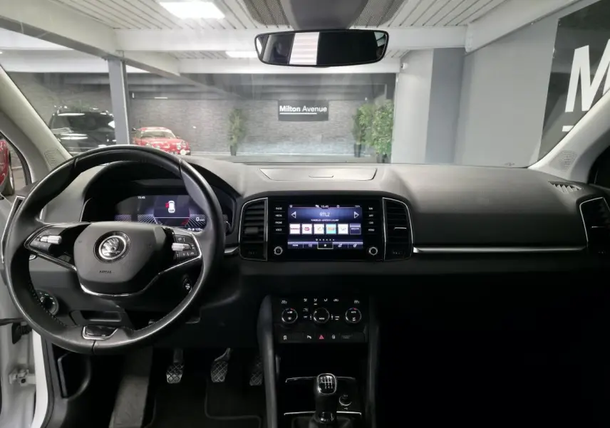 Intérieur du Skoda Karoq blanc 2024, vue frontale sur tableau de bord, volant multifonction et écran tactile central.