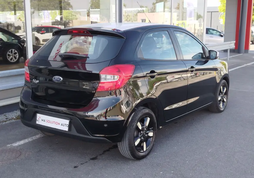 Ford Ka+ noir Shadow avec toit blanc, vue 3/4 arrière droit, jantes biton et feux arrière rouges visibles.