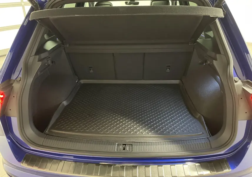 Coffre ouvert vu de l'arrière d'un Volkswagen Tiguan Bleu Lapiz, avec tapis de protection noir et seuil métallique.