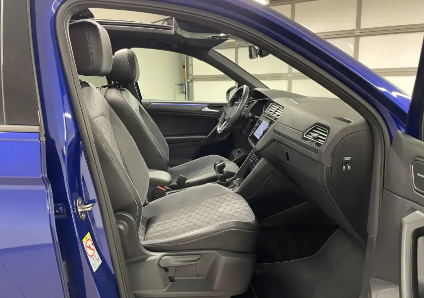 Vue intérieure côté conducteur du Volkswagen Tiguan Bleu Lapiz 2022, sièges tissu et cuir noirs avec surpiqûres blanches.