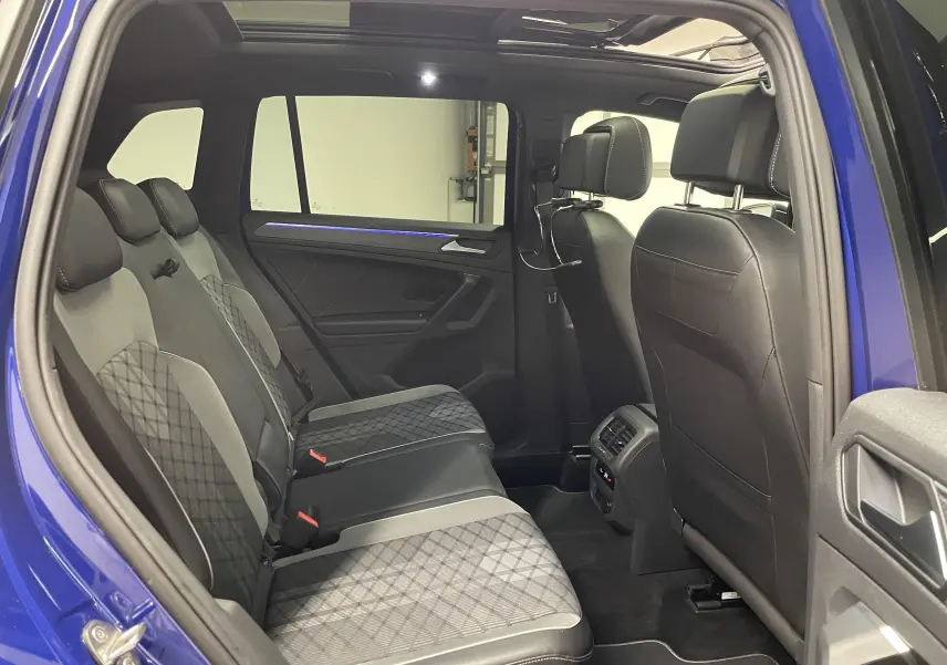 Vue intérieure côté gauche des sièges arrière en tissu et cuir noir du Volkswagen Tiguan Bleu Lapiz avec toit panoramique ouvert.