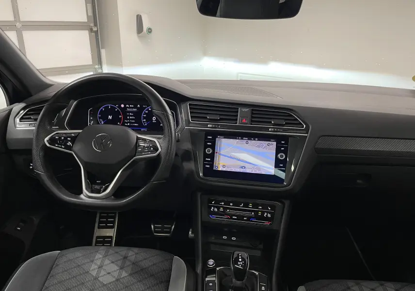 Vue intérieure avant du Volkswagen Tiguan 2022, tableau de bord noir avec écran tactile et volant multifonction.