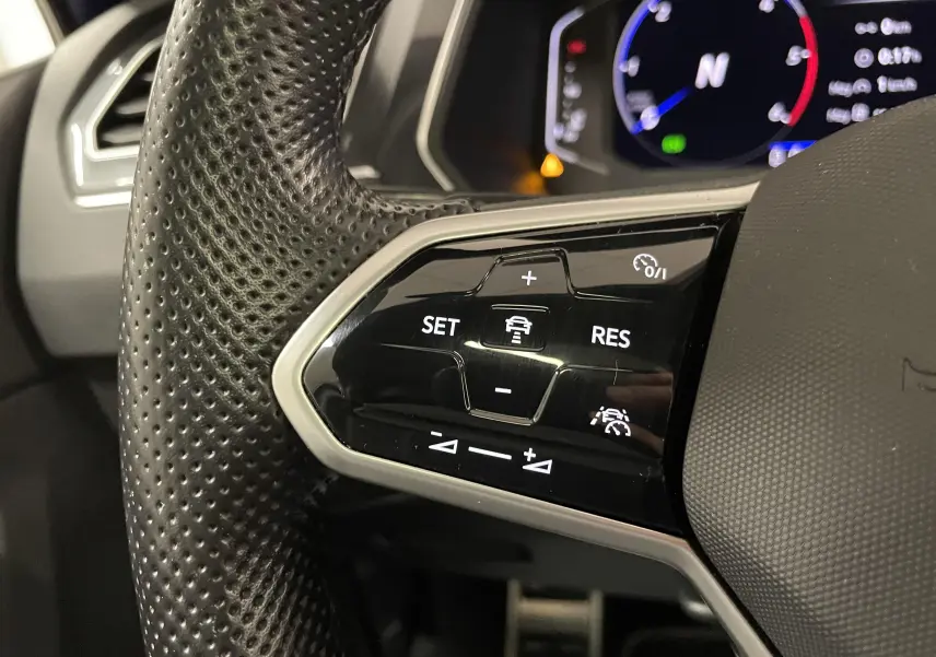 Gros plan sur les commandes du volant perforé noir du Volkswagen Tiguan 2022, affichage numérique en arrière-plan.