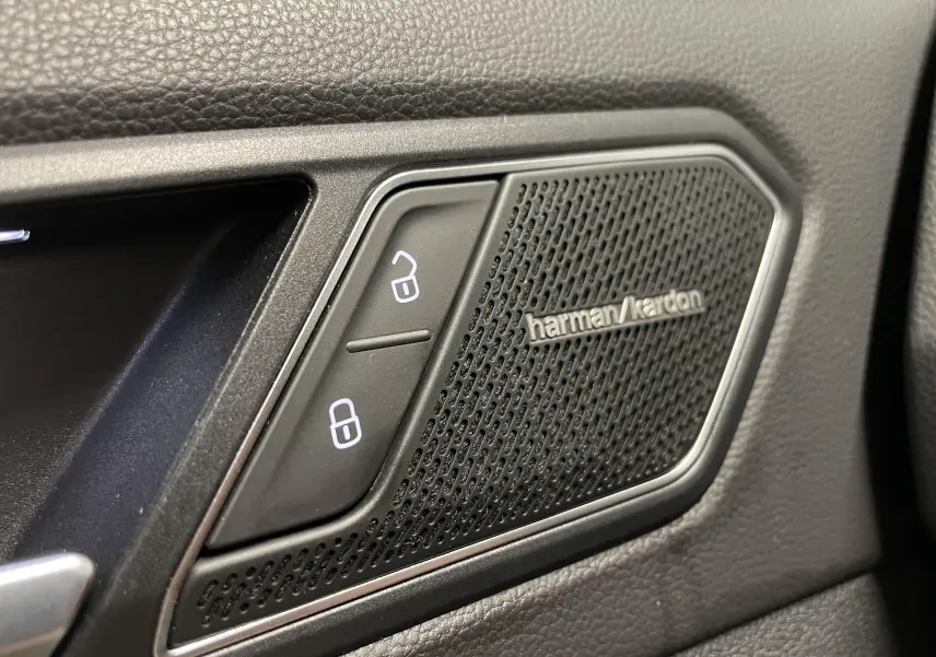 Gros plan sur la grille de haut-parleur Harman Kardon et les boutons de verrouillage dans l'habitacle noir du Volkswagen Tiguan.