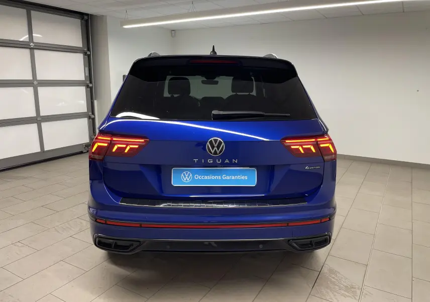 Vue arrière d'un Volkswagen Tiguan Bleu Lapiz avec feux LED allumés et vitres arrière surteintées dans un garage.