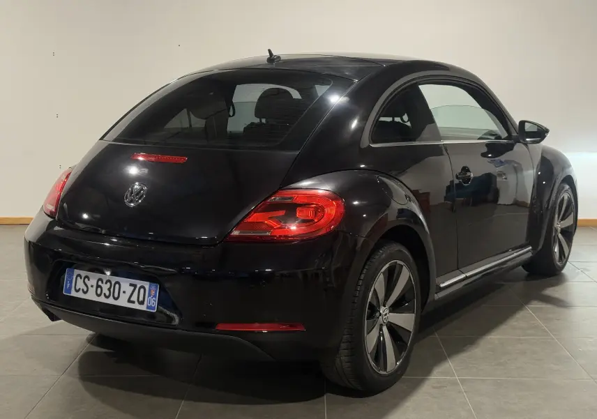 Vue 3/4 arrière droite d'une Volkswagen Coccinelle noire 2013 Fender Edition avec jantes spécifiques et feux arrière allumés.