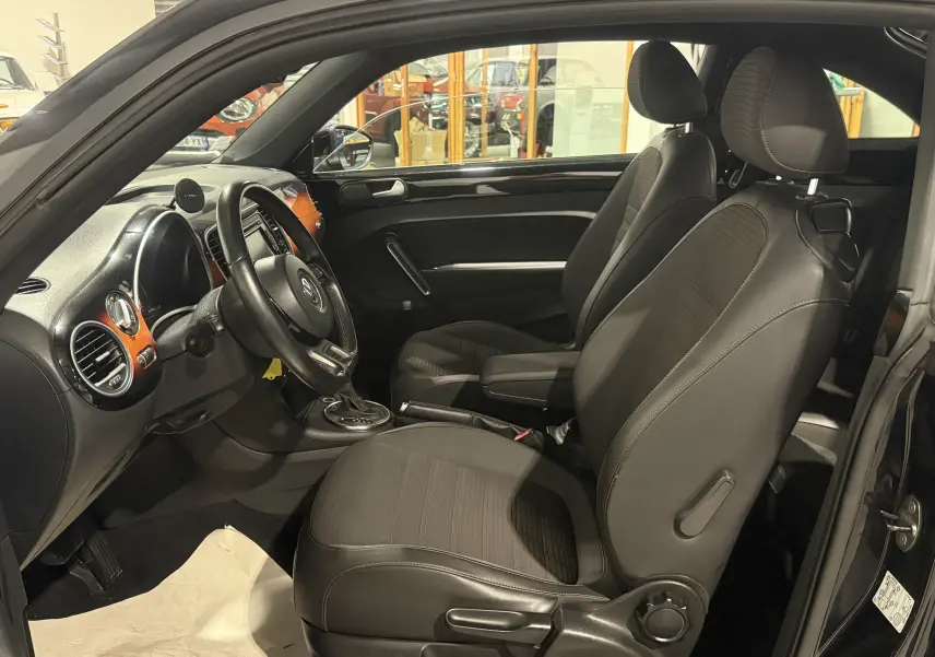 Vue intérieure côté conducteur de la Volkswagen Coccinelle noire 2013 avec sellerie noire et inserts bois sur tableau de bord.
