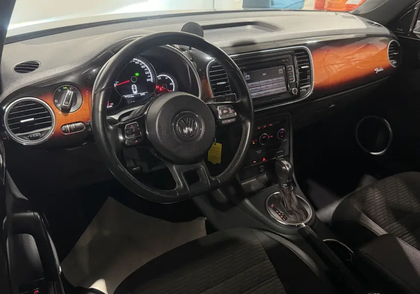 Vue intérieure côté conducteur de la Volkswagen Coccinelle noire 2013, tableau de bord avec inserts bois et boîte auto.