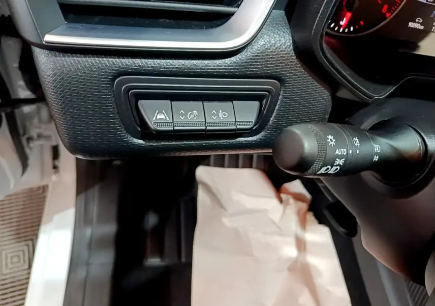 Gros plan sur les commandes d'assistance et réglage des phares côté gauche du tableau de bord d'une Renault Clio blanche.