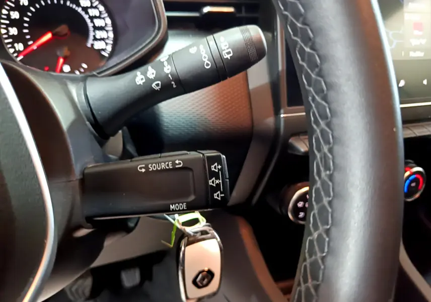 Gros plan sur le volant cuir et les commandes au volant d'une Renault Clio blanche, tableau de bord partiellement visible.