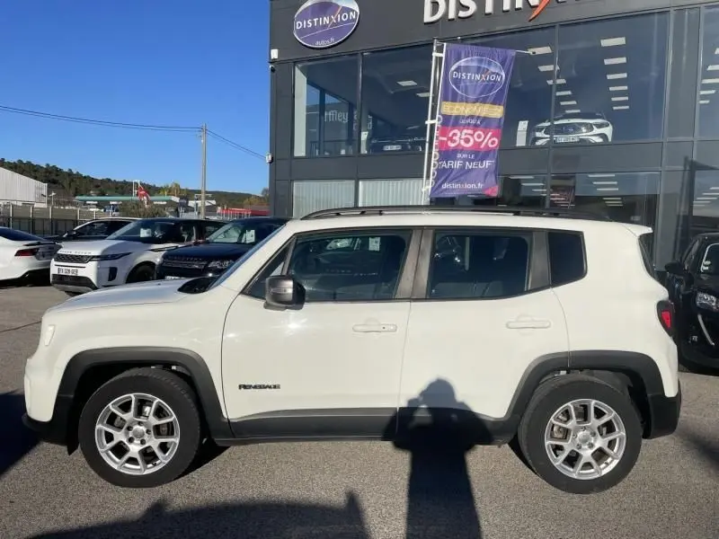 Vue de profil côté gauche d'un Jeep Renegade blanc 2019 Limited essence, avec jantes alliage et barres de toit noires.