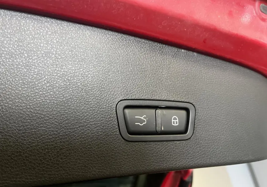 Gros plan sur bouton d’ouverture de coffre et verrouillage, intérieur noir, bord de coffre rouge Alfa Romeo Tonale 2024.