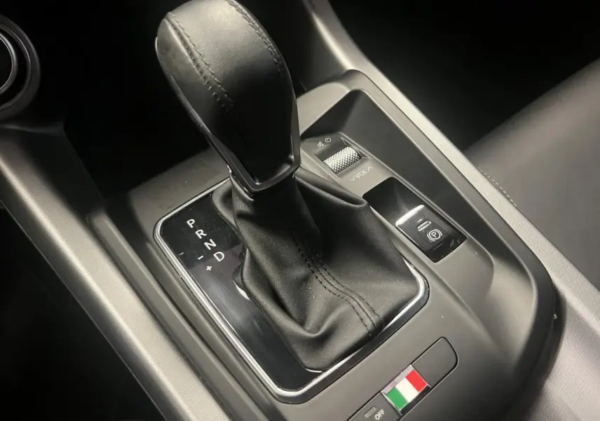 Gros plan sur la console centrale noire de l'Alfa Romeo Tonale avec levier de vitesse automatique et logo tricolore italien.